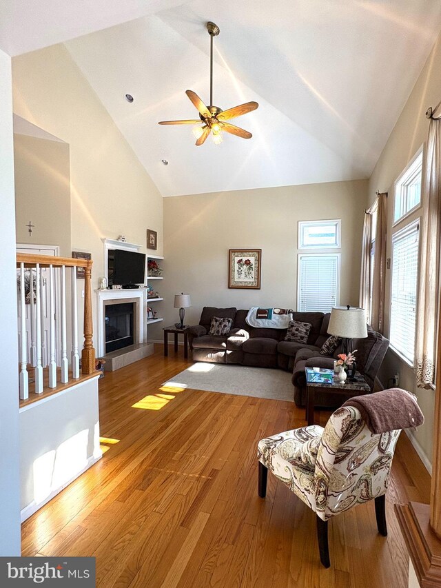 living area with a ceiling fan, a fireplace, high vaulted ceiling, and wood finished floors