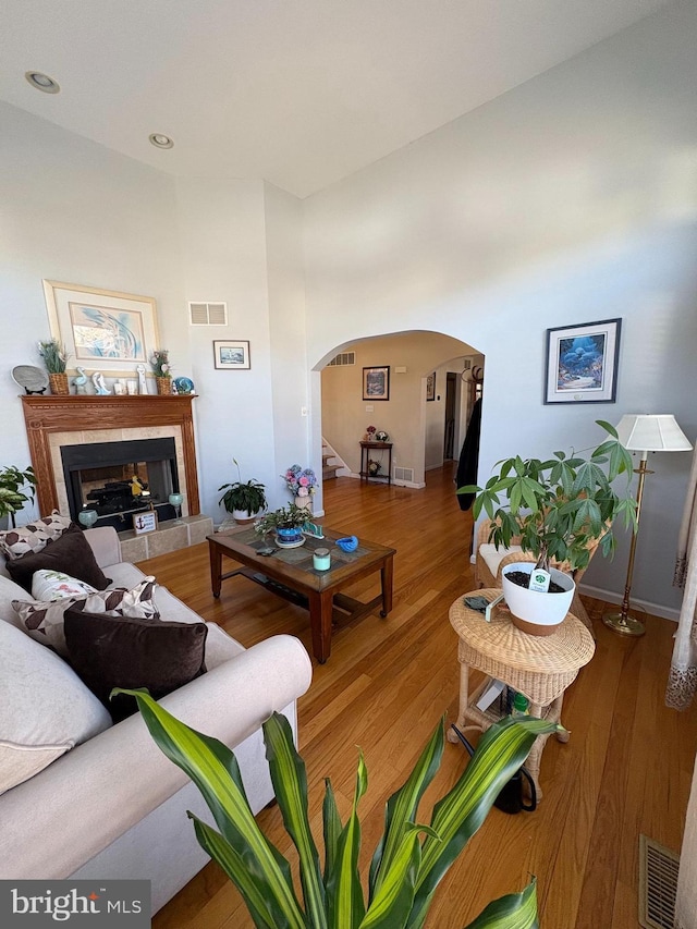 living area featuring arched walkways, a tile fireplace, wood finished floors, and visible vents