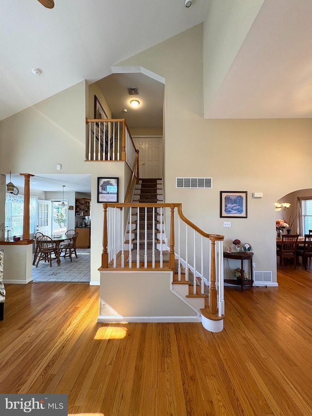 stairway with arched walkways, visible vents, and wood finished floors