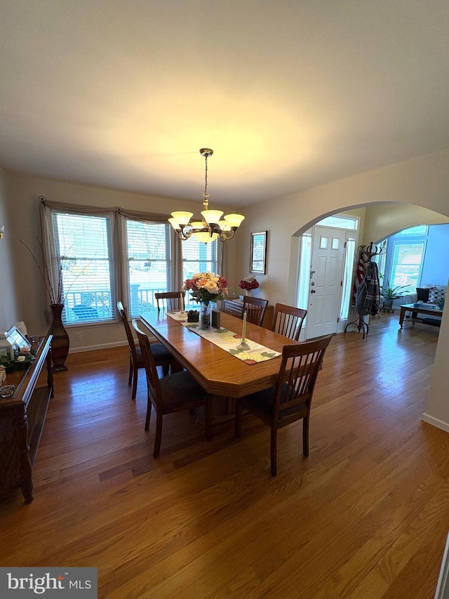 dining area with baseboards, a notable chandelier, arched walkways, and wood finished floors