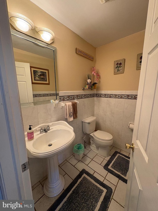 half bathroom with wainscoting, toilet, tile patterned floors, a sink, and tile walls