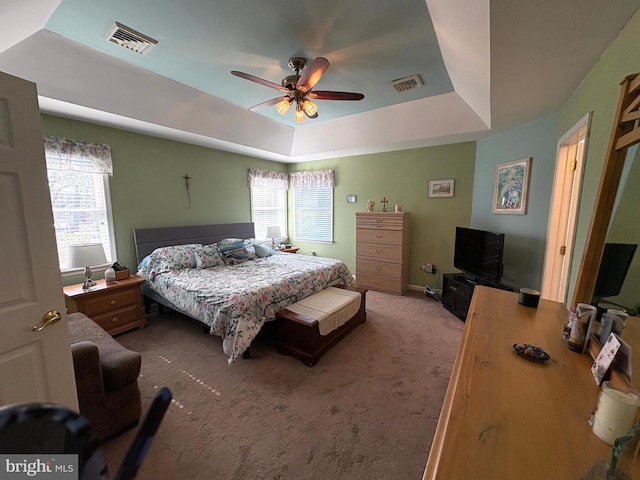 bedroom with a ceiling fan, a tray ceiling, visible vents, and light carpet