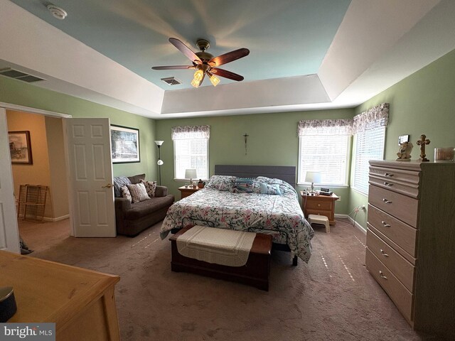 carpeted bedroom featuring a ceiling fan, a tray ceiling, visible vents, and baseboards