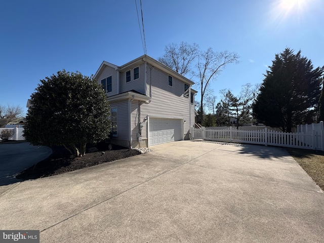 view of side of property featuring concrete driveway, an attached garage, and fence