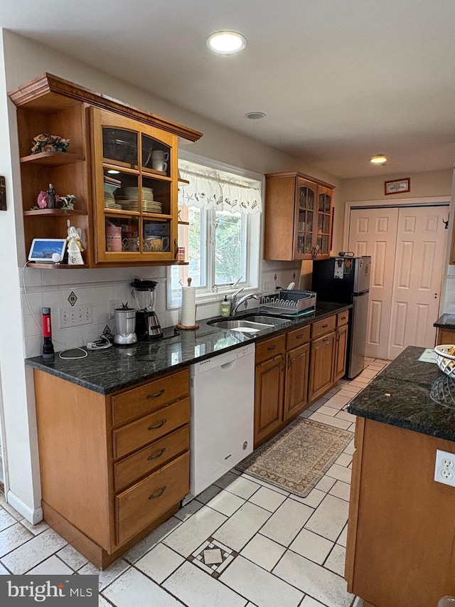 kitchen with white dishwasher, brown cabinetry, a sink, and freestanding refrigerator