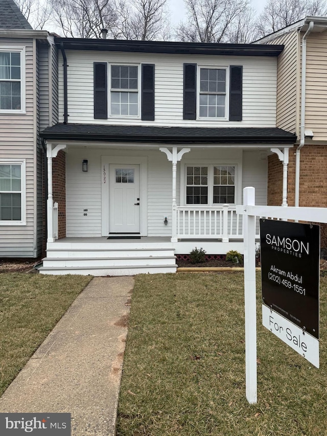 view of front facade with a porch, a front yard, and brick siding