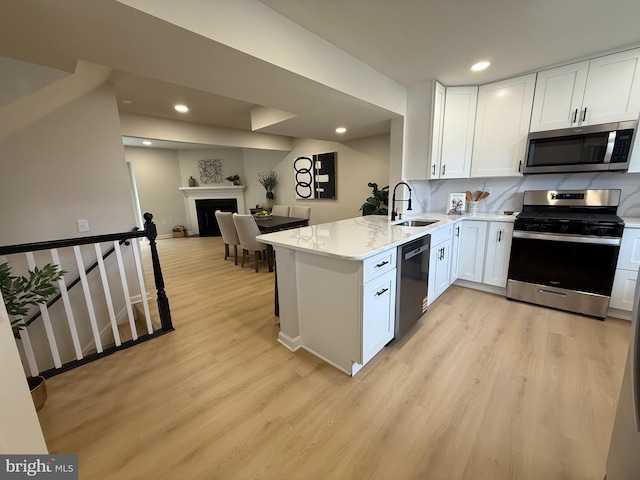 kitchen with light wood finished floors, stainless steel appliances, white cabinets, a sink, and a peninsula