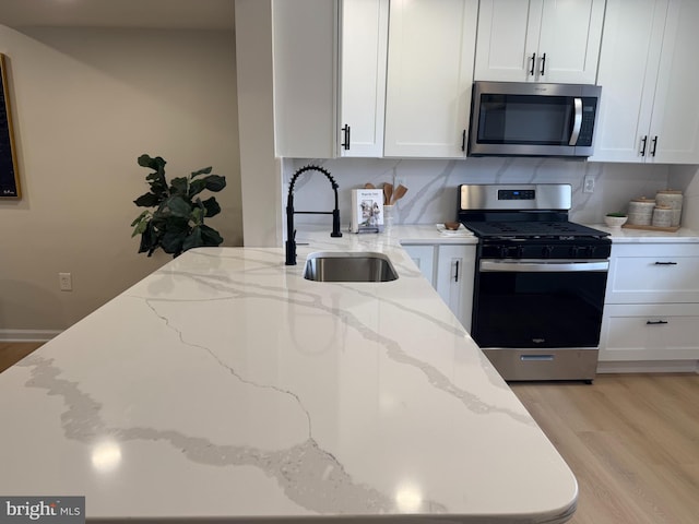 kitchen with light wood finished floors, tasteful backsplash, appliances with stainless steel finishes, white cabinetry, and a sink