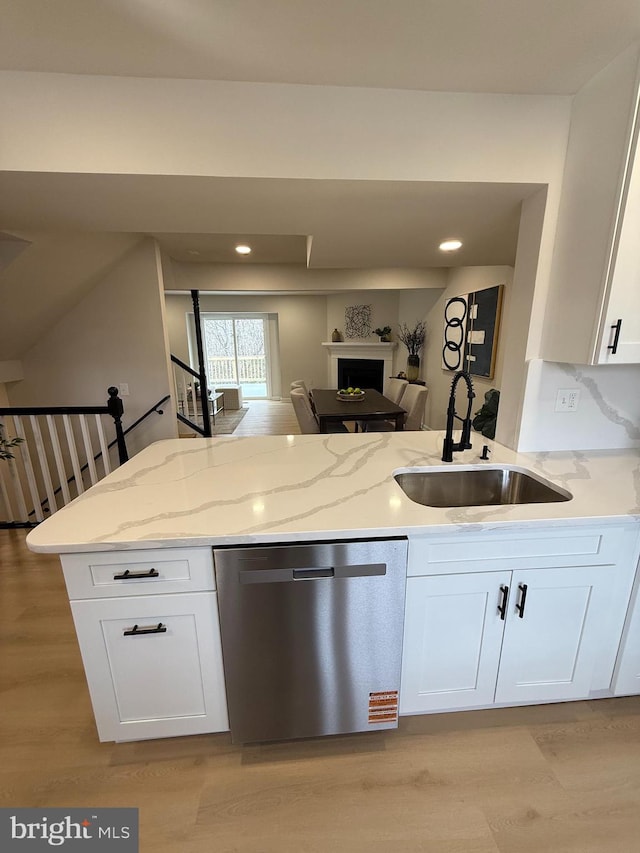 kitchen featuring light wood finished floors, white cabinets, a sink, light stone countertops, and dishwasher