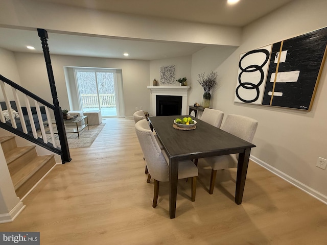 dining area with light wood-style flooring, recessed lighting, a fireplace, baseboards, and stairway