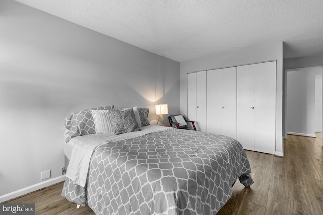 bedroom with a closet, a textured ceiling, baseboards, and wood finished floors