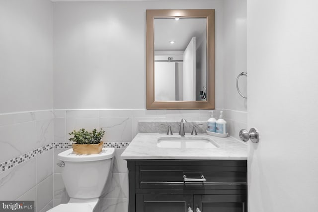 bathroom featuring toilet, vanity, and tile walls