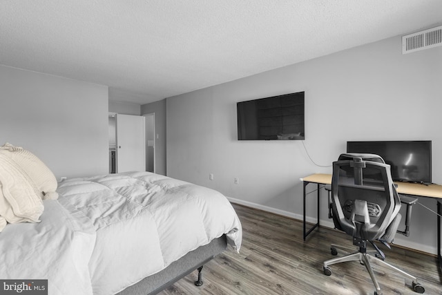 bedroom with visible vents, a textured ceiling, baseboards, and wood finished floors