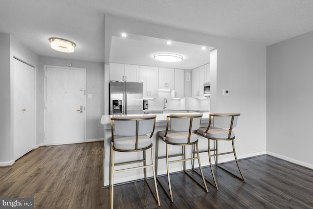 kitchen featuring dark wood-type flooring, white cabinetry, a kitchen breakfast bar, light countertops, and appliances with stainless steel finishes