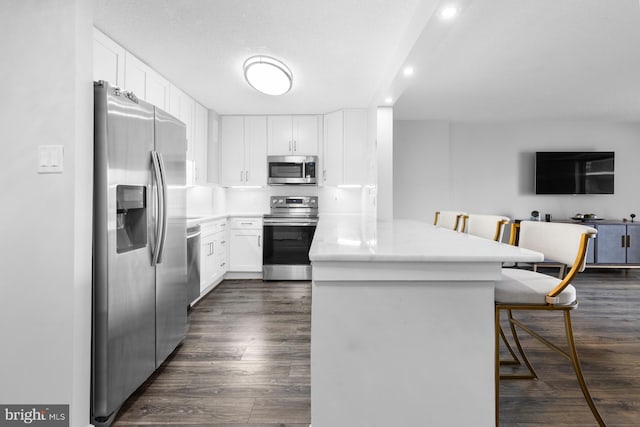 kitchen featuring dark wood-style floors, appliances with stainless steel finishes, white cabinetry, a peninsula, and a kitchen breakfast bar