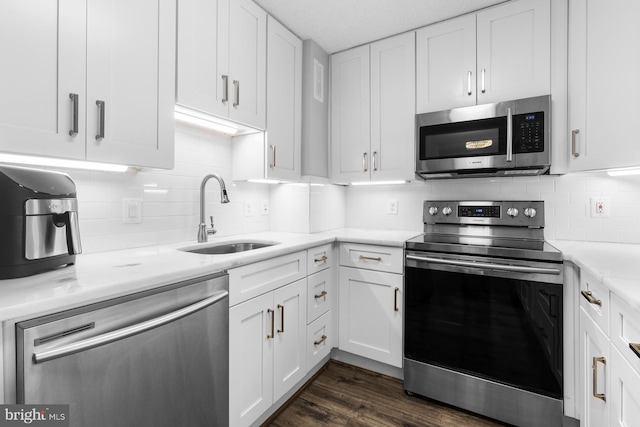 kitchen with dark wood-type flooring, appliances with stainless steel finishes, white cabinets, and a sink