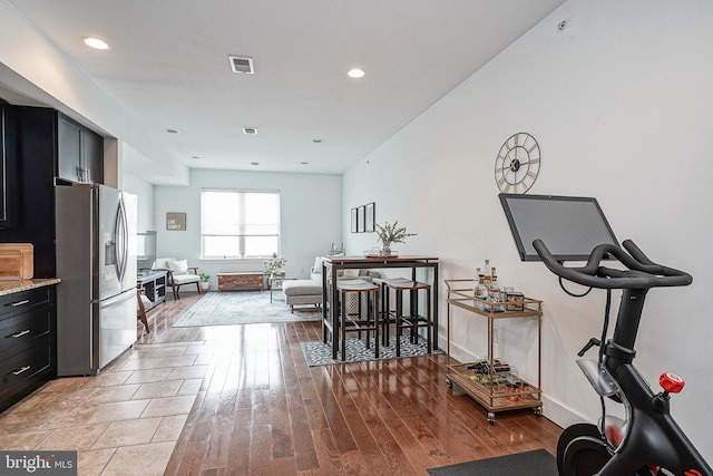 kitchen with dark cabinets, light wood-type flooring, stainless steel fridge, and visible vents