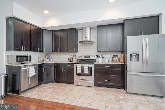 kitchen with appliances with stainless steel finishes, backsplash, a sink, and wall chimney range hood