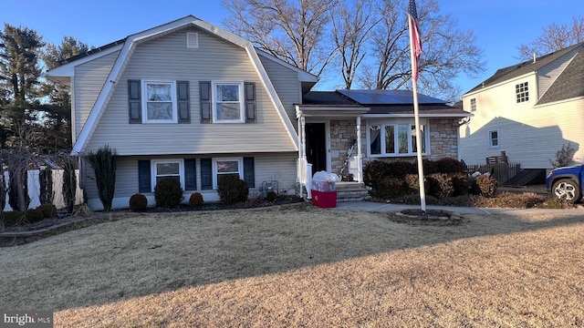 view of front of house with stone siding, fence, a gambrel roof, and solar panels