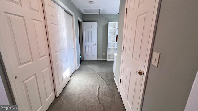 hall with dark carpet, attic access, and baseboards