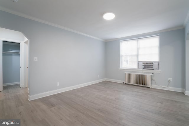 empty room featuring arched walkways, wood finished floors, baseboards, ornamental molding, and radiator