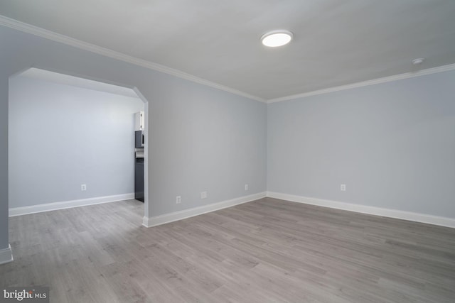 empty room featuring arched walkways, crown molding, baseboards, and light wood-style floors