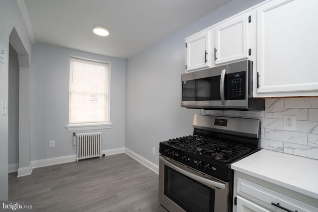 kitchen featuring stainless steel appliances, tasteful backsplash, radiator heating unit, white cabinetry, and baseboards