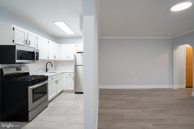 kitchen with arched walkways, stainless steel appliances, decorative backsplash, white cabinets, and a sink