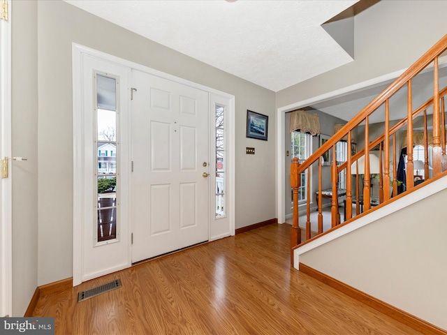 foyer entrance with visible vents, stairway, baseboards, and wood finished floors