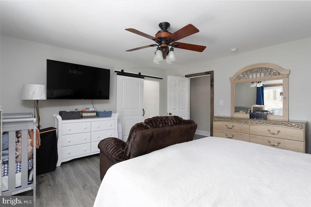 bedroom with ceiling fan, a barn door, and wood finished floors