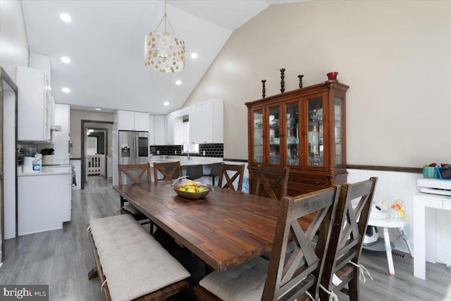 dining area with a wainscoted wall, high vaulted ceiling, light wood-style flooring, recessed lighting, and a notable chandelier