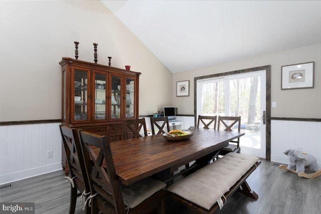 dining space with a wainscoted wall, wood finished floors, and vaulted ceiling