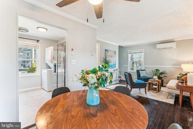 dining area with a textured ceiling, a wall mounted AC, washer / clothes dryer, wood-type flooring, and crown molding