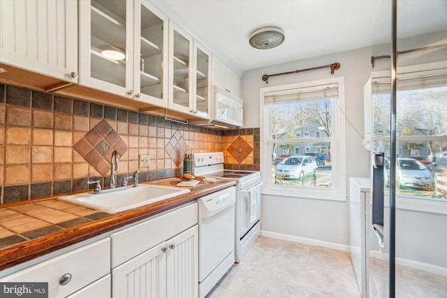 kitchen featuring white appliances, tasteful backsplash, glass insert cabinets, white cabinetry, and a sink