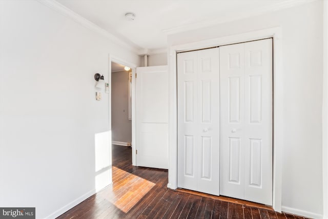 unfurnished bedroom with ornamental molding, a closet, dark wood-type flooring, and baseboards