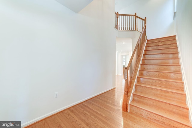 stairs featuring a towering ceiling, baseboards, and wood finished floors