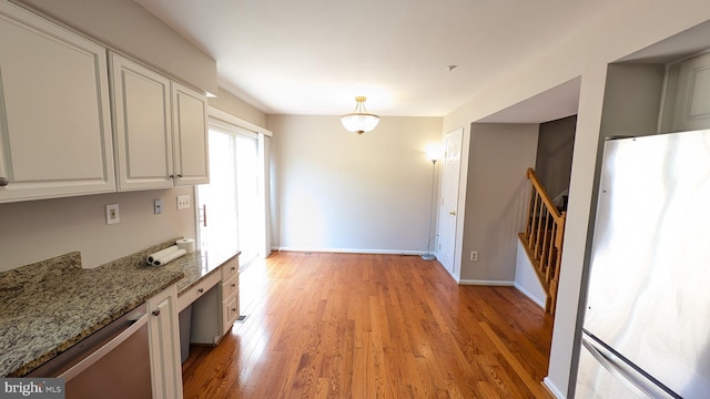 kitchen with light stone counters, baseboards, freestanding refrigerator, white cabinetry, and light wood-type flooring