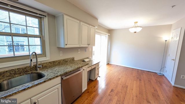 kitchen featuring light stone countertops, white cabinetry, a sink, light wood-style floors, and stainless steel dishwasher