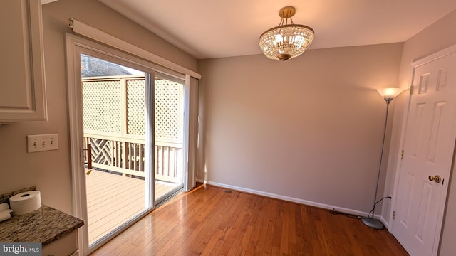 unfurnished room featuring baseboards, an inviting chandelier, and light wood-style flooring