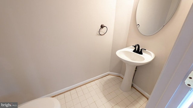 half bathroom with a sink, baseboards, toilet, and tile patterned flooring