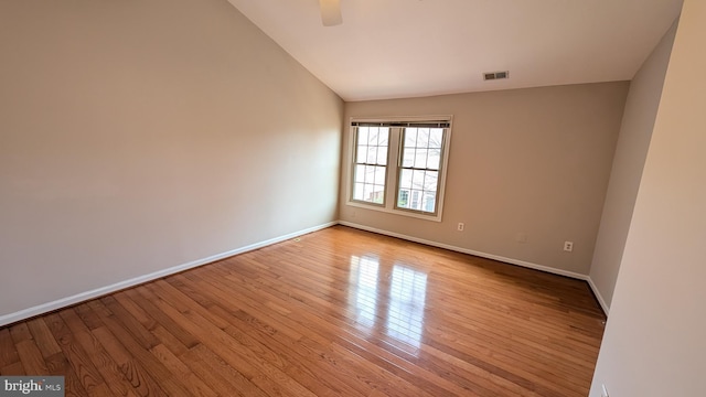 unfurnished room with visible vents, lofted ceiling, a ceiling fan, hardwood / wood-style flooring, and baseboards