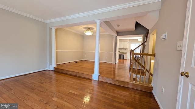 spare room featuring ornamental molding, wood-type flooring, decorative columns, baseboards, and stairs