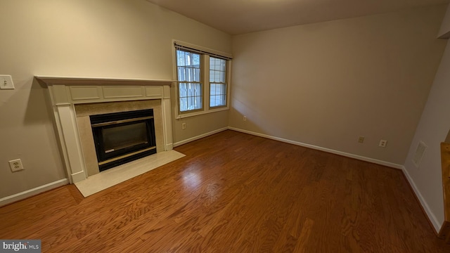 unfurnished living room with baseboards, wood finished floors, and a high end fireplace