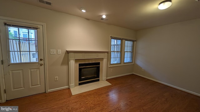 unfurnished living room featuring a fireplace with flush hearth, wood finished floors, visible vents, and baseboards