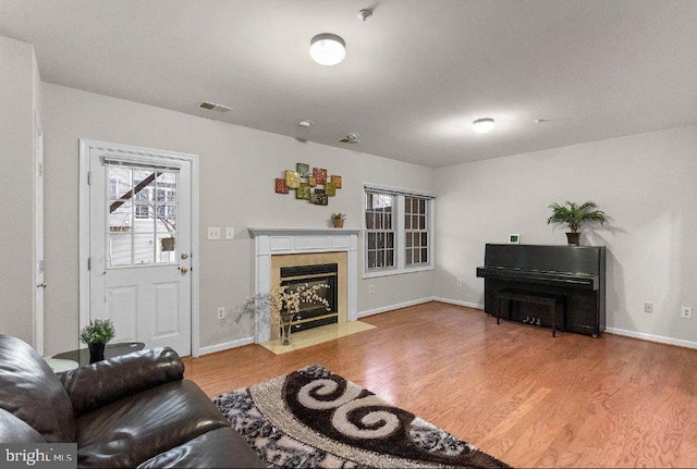 living room with a premium fireplace, visible vents, baseboards, and wood finished floors