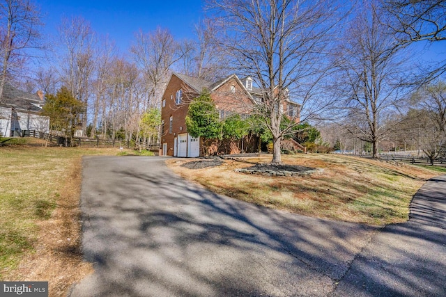 view of side of home featuring brick siding, an attached garage, fence, a lawn, and driveway