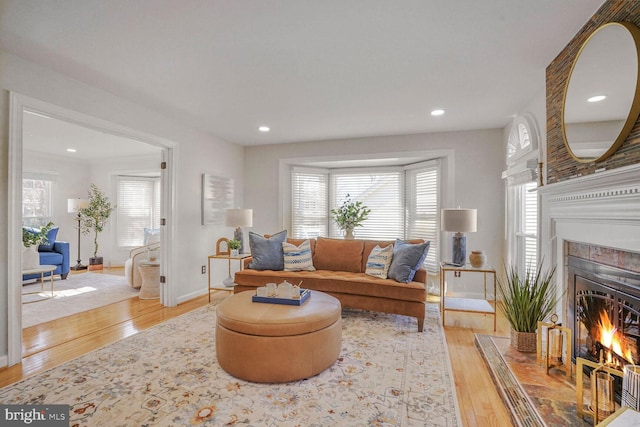 living room with a warm lit fireplace, recessed lighting, baseboards, and light wood-style floors