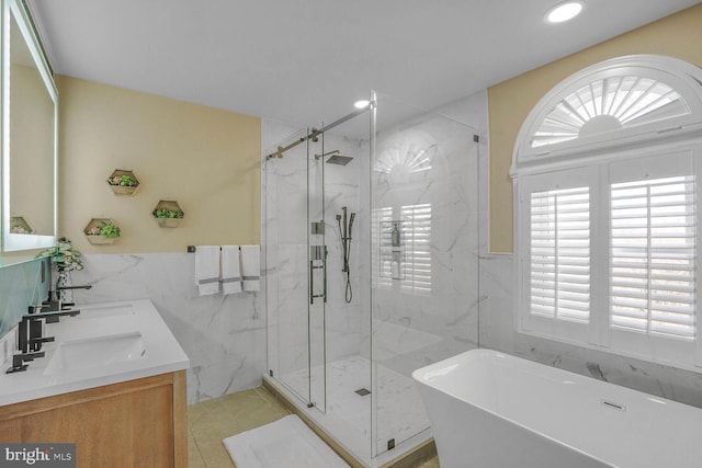 full bathroom with tile walls, a marble finish shower, double vanity, a sink, and a freestanding tub