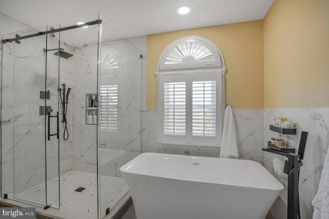 full bathroom featuring a marble finish shower, tile walls, a freestanding bath, and recessed lighting