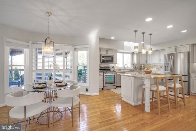 kitchen featuring a chandelier, stainless steel appliances, a sink, light wood-type flooring, and tasteful backsplash